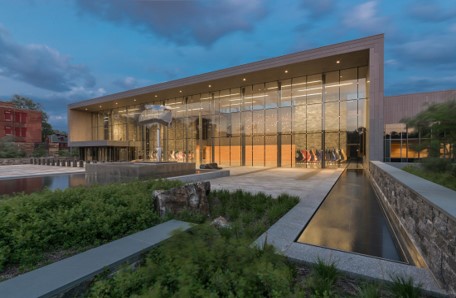 Nupress facade — illuminated glass pavilion with reflecting pools at dusk